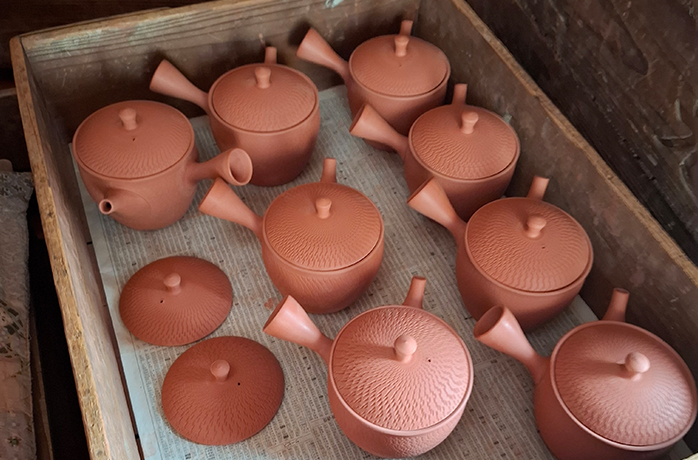 Mehrere unglasierte Kyusu-Teekannen aus rotem Ton, sorgfältig aufgereiht in einer Holzkiste Mehrere unglasierte Kyusu-Teekannen aus rotem Ton, sorgfältig aufgereiht in einer Holzkiste
