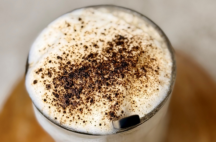 Hojicha Latte im Glas mit Milchschaum, bestäubt mit Hojicha-Pulver, Detailaufnahme von oben