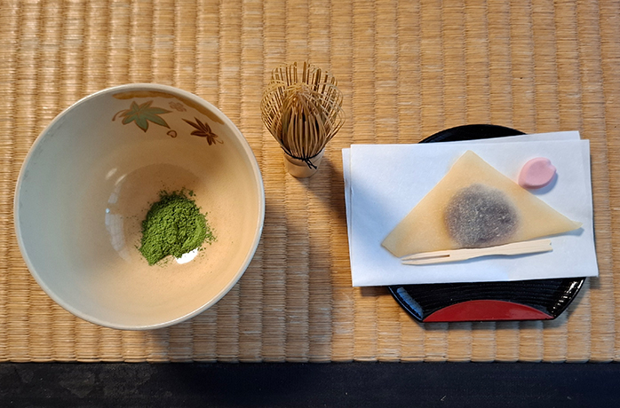 Matcha-Schale mit grünem Pulver, Bambusbesen und Wagashi-Gebäck auf Tatami-Matte – Vorbereitung zur Teezeremonie