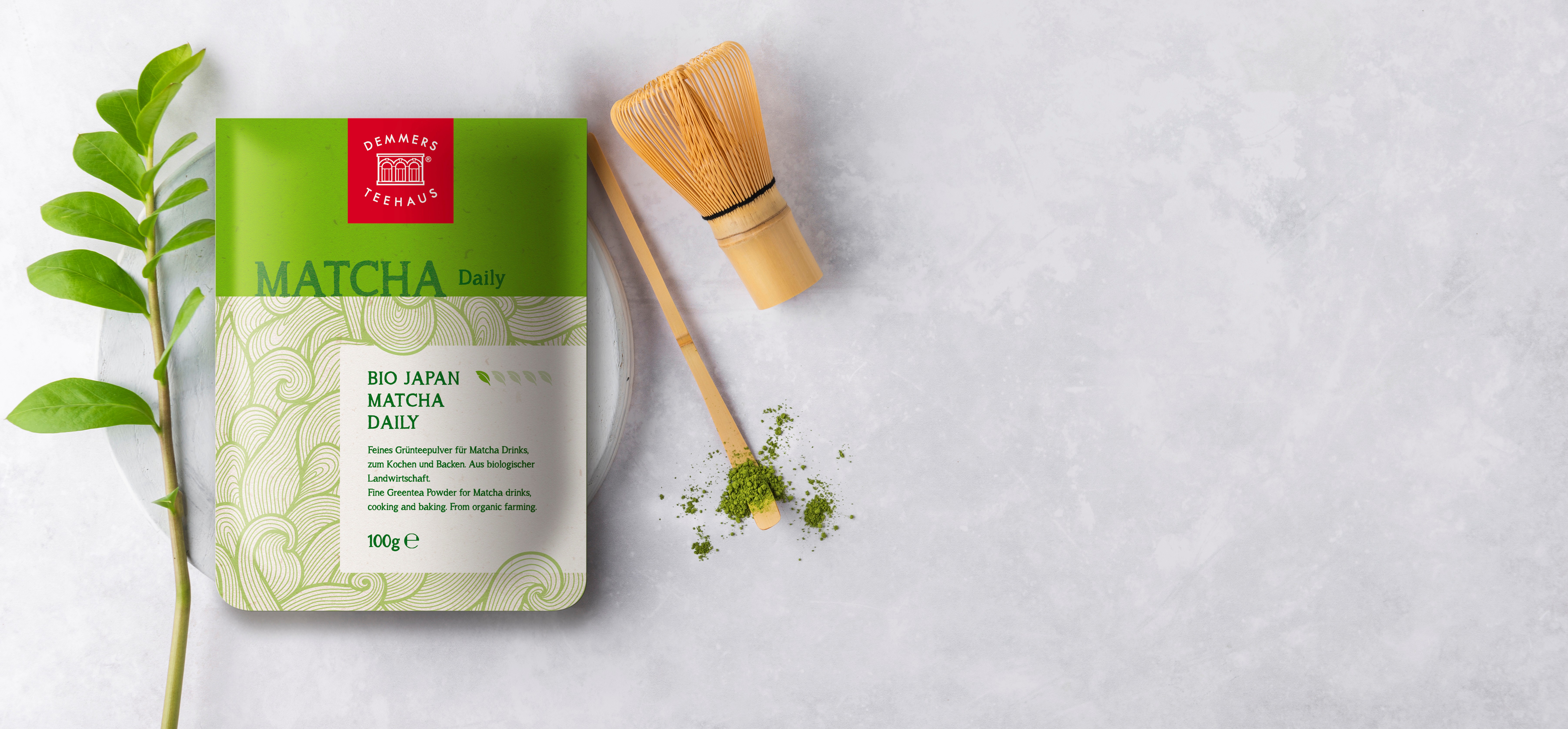 Demmers Teehaus BIO Japan Matcha Daily 100g verpackt auf Teller mit Besen, Löffel und Blatt