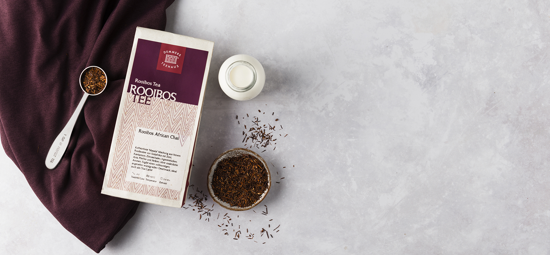 Demmers Teehaus Rooibos Tee Rooibos African Chai verpackt  auf Tuch mit Teemaßlöffel, losem Tee und Milchflasche