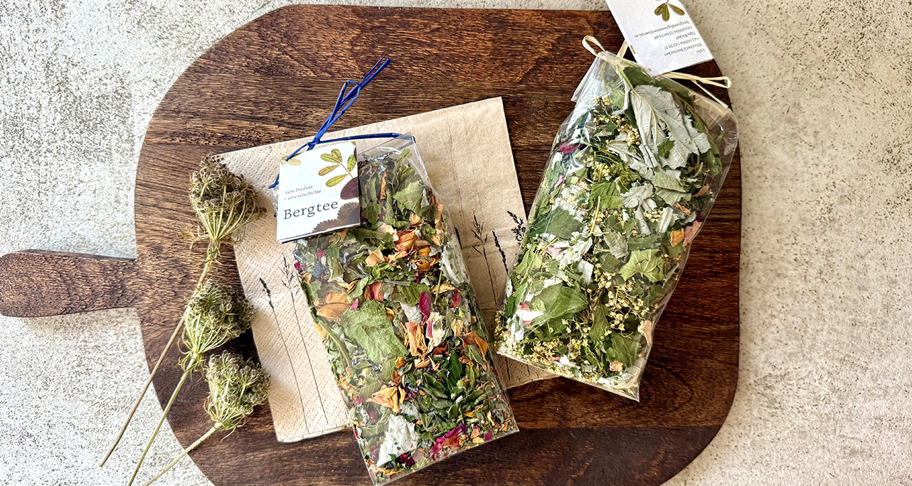 Abgepackter Bergtee in transparenten Beuteln mit sichtbaren Blättern und Blüten, dekorativ auf Holzbrett arrangiert