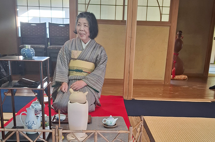 Japanische Teemeisterin im Kimono bereitet auf Tatami-Matten eine Teezeremonie mit Kanne und Teeschalen vor