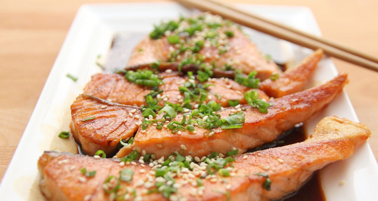 Lachsteaks mit Jungzwiebel garniert angerichtet auf einem weißen Teller