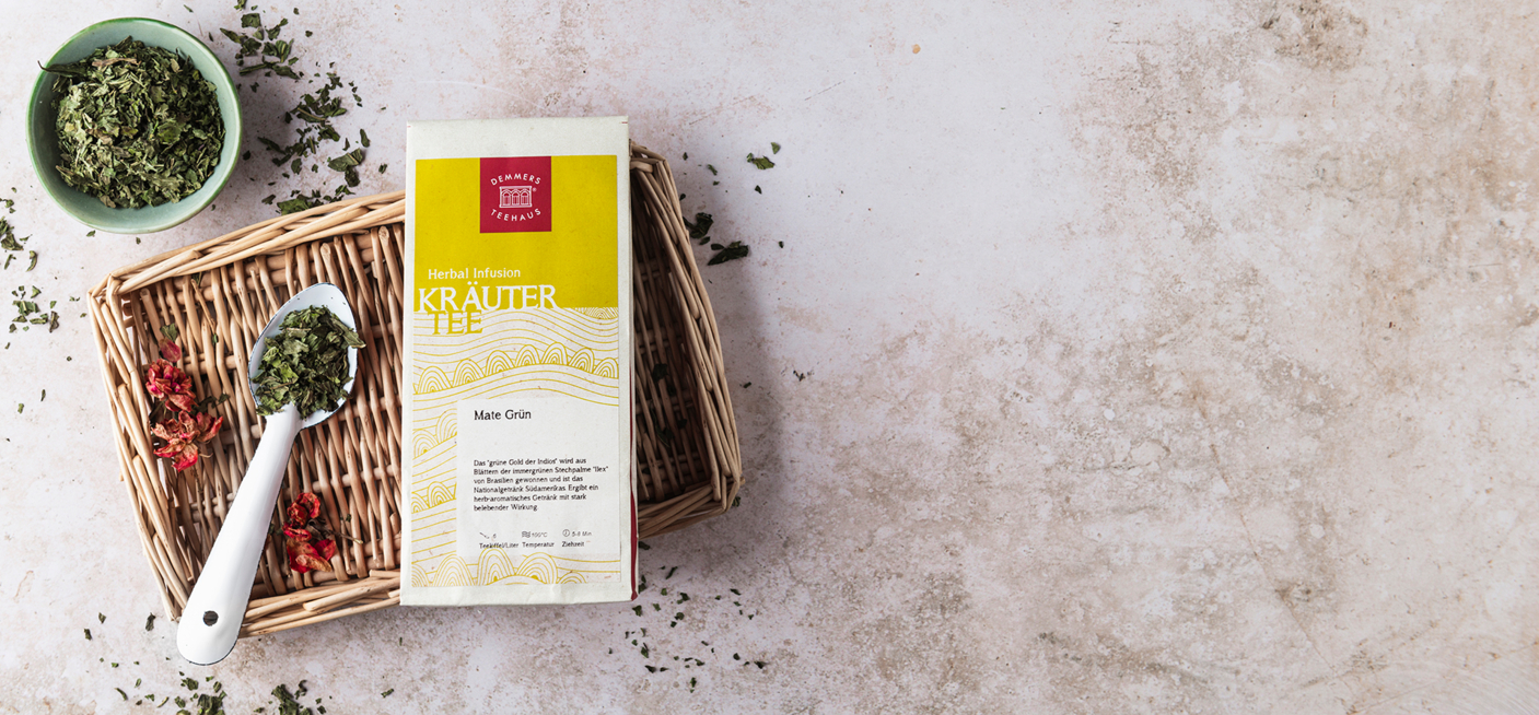 Demmers Teehaus Mate Tee Mate grün verpackt auf Korbtablet mit Löffel und losem Tee