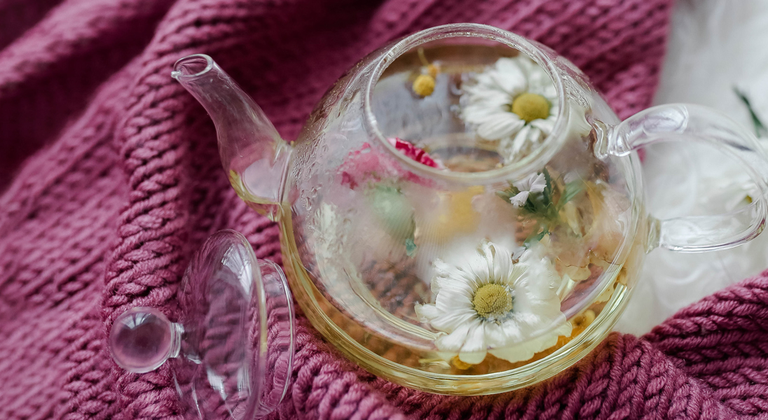 Glaskanne mit Kräutern und Blumen auf rosa Schal