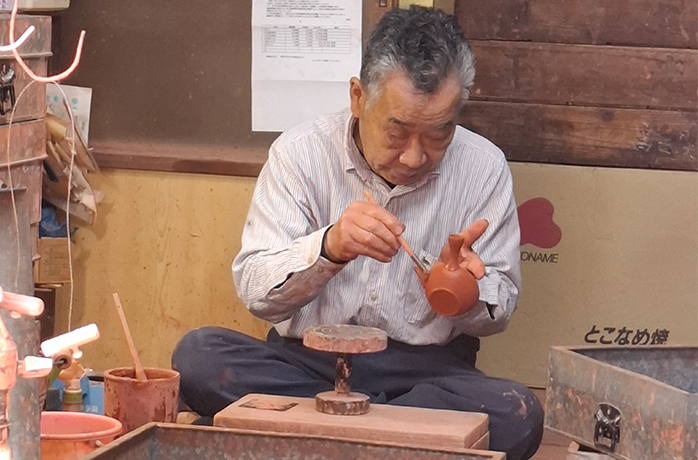 Japanischer Keramiker beim letzten Feinschliff an einer handgefertigten Kyusu-Teekanne Japanischer Keramiker beim letzten Feinschliff an einer handgefertigten Kyusu-Teekanne