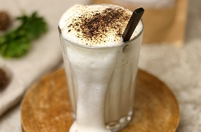 Hohes Glas Hojicha Latte mit Milchschaum und Hojicha-Pulver, schwarzer Löffel, auf Holzuntersetzer